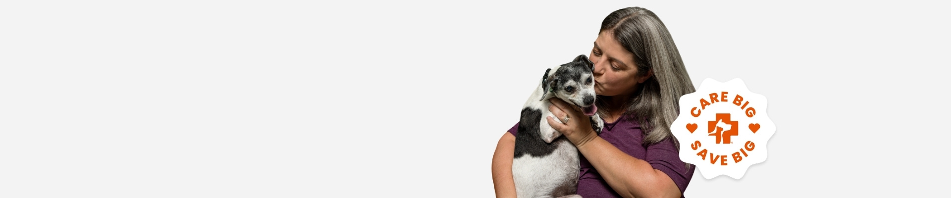 A woman holding and kissing her small senior dog