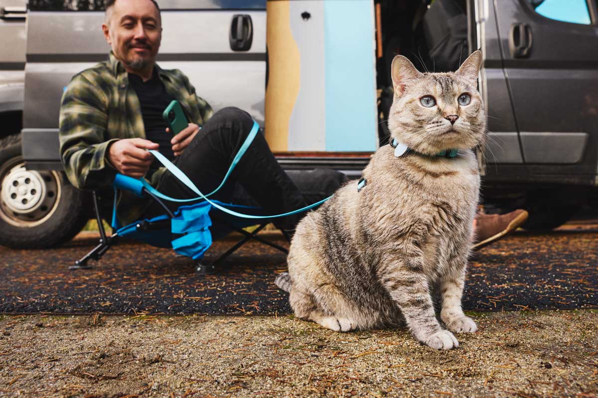 A man sitting outside his camper with a cat on a blue leash